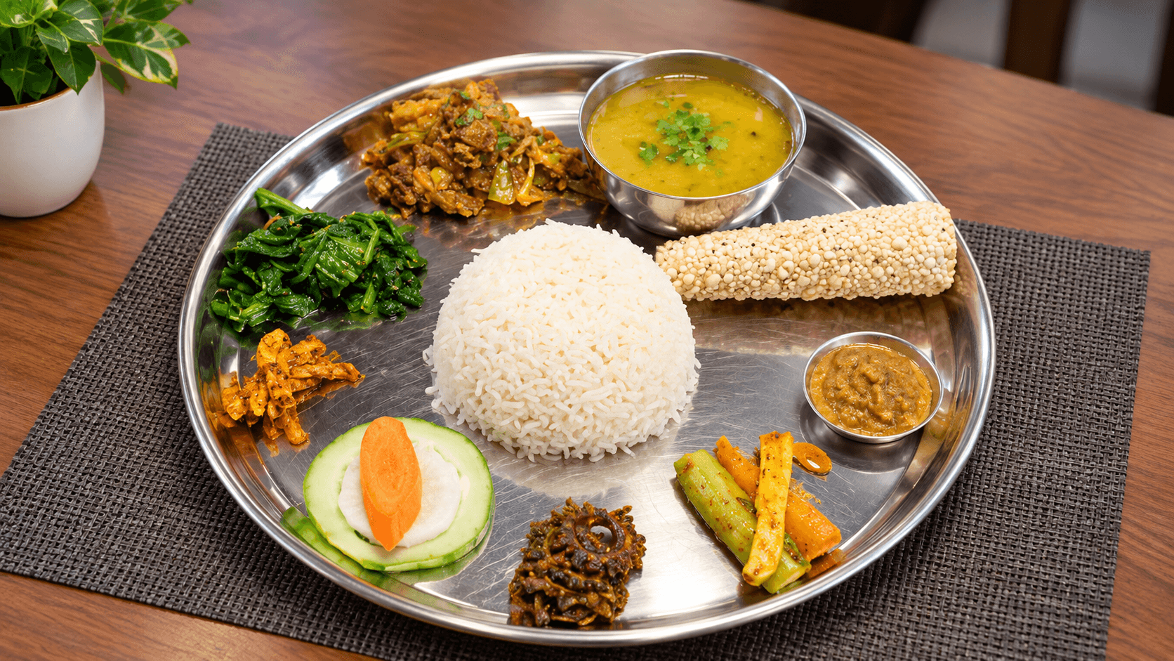 Traditional Nepali thali with rice, dal, vegetable curry, greens, pickles, and papad on a steel plate